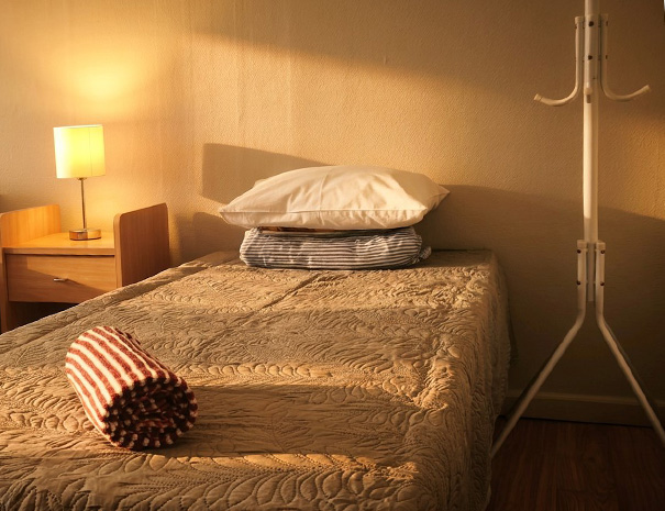 Close-up of a bed with a soft clean towel and one of the two practical clothing racks in the large room at Hostel Lõuna.