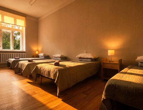Large room for 5-6 people on the 2nd floor of Hostel Lõuna featuring fresh towels on comfortable beds, nightstands, and cozy lighting with a park view.