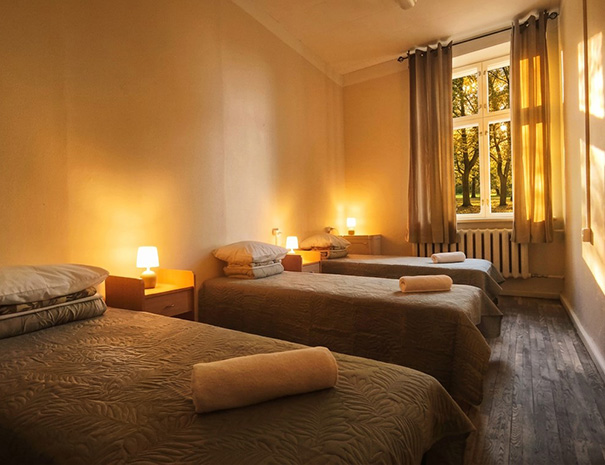 Triple room on the 2nd floor of Hostel Lõuna featuring three comfortable beds with soft towels, nightstands, and cozy lighting with a park view.