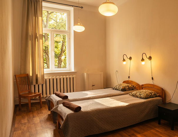 Twin room on the 2nd floor of Hostel Lõuna featuring soft towels on two single beds, nightstands, warm, cozy retro lighting and park view.