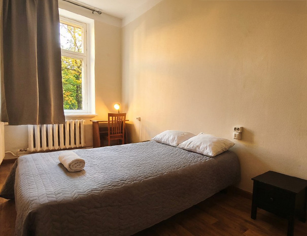 Ülevaade Hostel Lõuna 2. korruse ühekohalisest toast mugava voodi, rätiku, kirjutuslaua ja pargivaatega.