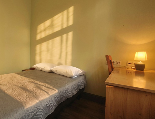 Hostel Lõuna ühekohaline tuba mugava voodi, kirjutuslaua ja sooja hubase valgustusega õhtusel ajal.