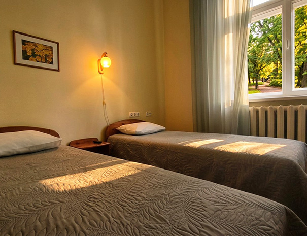 Hostel Lõuna kahe eraldi voodiga twin tuba hubase valgustusega, taustal aken vaatega rohelisele pargile.